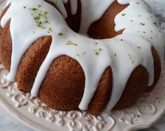 May include: A white frosted bundt cake with green sprinkles on top, sitting on a white plate with a decorative design.