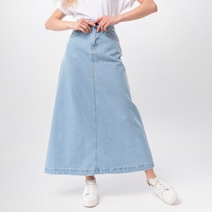 May include: A woman wearing a white t-shirt and a light blue denim maxi skirt. She is smiling and has curly blonde hair.