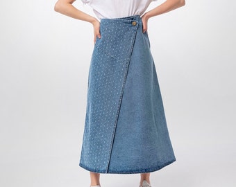 May include: A woman with curly blonde hair is wearing a white t-shirt and a blue denim skirt with a white dotted pattern. She is standing with her hands on her hips and smiling at the camera.