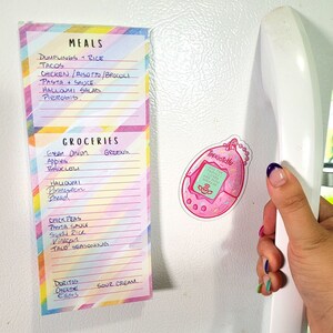 May include: A pink and white refrigerator magnet with a cartoon image of a Tamagotchi. The text on the magnet reads "All the things I love are now vintage".