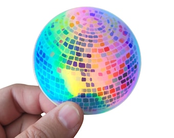 May include: A rainbow iridescent disco ball sticker. The sticker is round and has a mirrored surface with small squares.