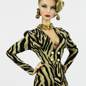 May include: A doll wearing a black and brown zebra print jumpsuit with a gold chain necklace and gold earrings. The doll has blonde hair styled in a wave and red lipstick.