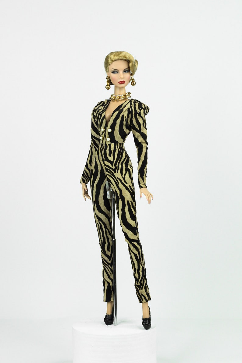 May include: A fashion doll wearing a black and tan zebra print jumpsuit with gold jewellery and black heels.