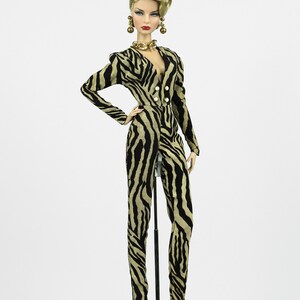 May include: A doll wearing a black and tan zebra print jumpsuit with gold jewellery and black high heels.