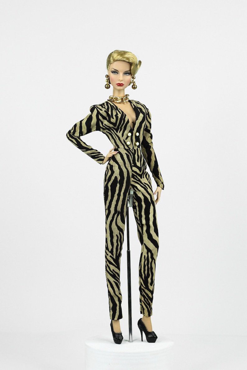 May include: A doll wearing a black and tan zebra print jumpsuit with gold jewellery and black high heels.
