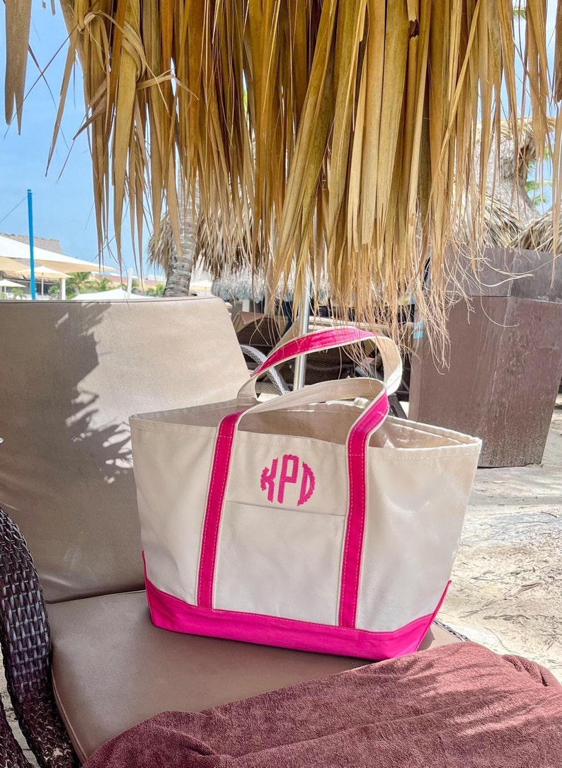 May include: A white canvas tote bag with pink trim and handles. The bag has a pink monogram "KPD" embroidered on the front.