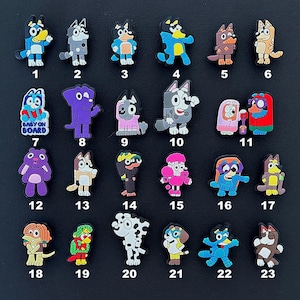 May include: A selection of 23 colourful cartoon character charms, each with a unique design and number. The charms feature various animals and figures in different poses and outfits. The background is a solid black.