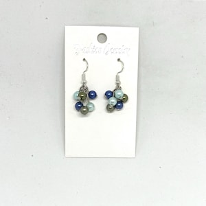 Puede incluir: Un par de pendientes colgantes de plata con cuentas azules, verdes y azul claro. Los pendientes están en una tarjeta blanca con el texto "Fashion Jewelry".