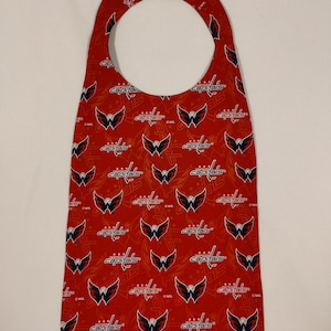 May include: Red door hanger with a white outline and a repeating pattern of the Washington Capitals NHL team logo. The logo is a red, white, and blue eagle with the word "Capitals" written below it.