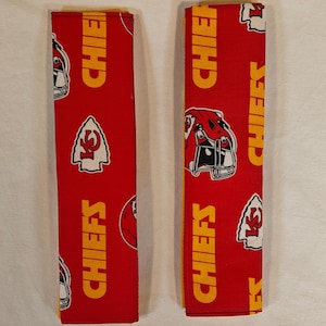 May include: Two red and yellow fabric seatbelt covers with the Kansas City Chiefs logo and the words "Chiefs" repeated on them.