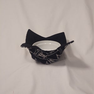 May include: Black fabric bowl cozy with a white bowl inside. The fabric has a white print of motorcycles and the words "RAIDERS" and "SHOOTERS".