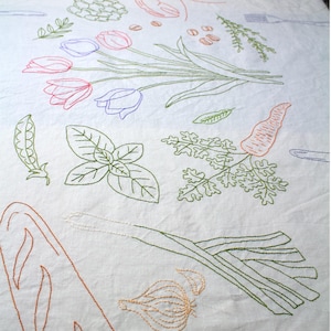 May include: A white tablecloth featuring colorful embroidered line art illustrations of food items including a lobster, tulips, a carrot, a leek, garlic, herbs, peas, and bread, interspersed with outlines of forks and knives across the fabric surface.