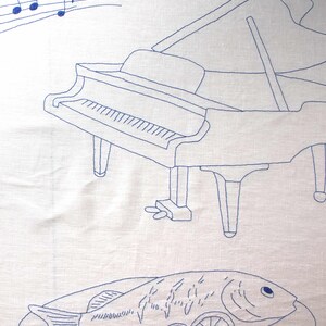 Detailed shot of the embroidery: blue musical staff with notes and a grand piano outline on a white linen background.