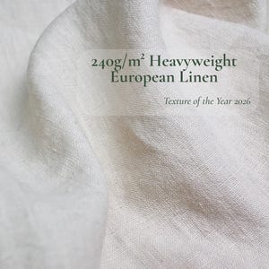 May include: Off-white heavyweight linen fabric with a visible woven texture and folds. The text printed on the fabric reads 240g/m&sup2; Heavyweight European Linen and Texture of the Year 2026. The material has a natural, matte, and slightly coarse appearance.