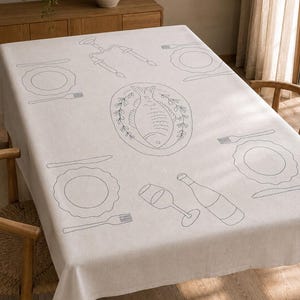 May include: A light beige rectangular tablecloth featuring dark grey line art illustrations of place settings, including plates, forks, knives, wine glasses, bottles, and a central platter with a fish surrounded by leafy branches.