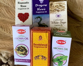 May include: Assortment of six small glass bottles of essential oils with labels. The bottles are arranged in two rows of three. The labels are white with black text and feature images of roses, dragons, elephants, sage, frankincense and myrrh, and mint. The bottles are all 10 ml.
