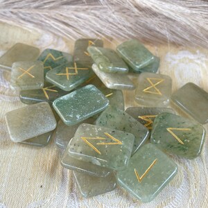 Puede incluir: Un conjunto de runas de piedra verde con s&iacute;mbolos dorados. Las runas tienen forma de rect&aacute;ngulos y est&aacute;n esparcidas sobre una superficie blanca.