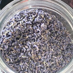 Op de afbeelding: Een glazen pot gevuld met gedroogde lavendelknoppen. De lavendel is lichtpaars van kleur en zit stevig in de pot.