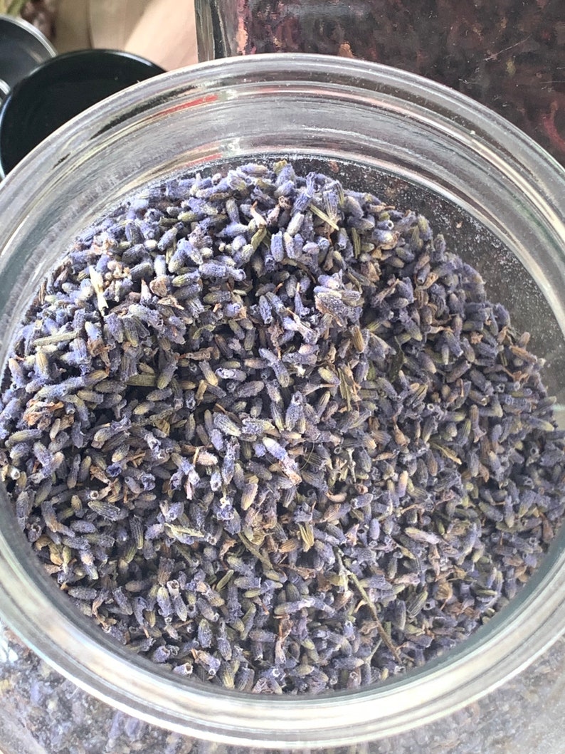 Op de afbeelding: Een glazen pot gevuld met gedroogde lavendelknoppen. De lavendel is lichtpaars van kleur en zit stevig in de pot.