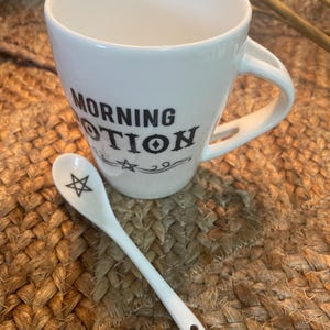 May include: White ceramic mug with black text that reads "Morning Potion" and a small white ceramic spoon with a black pentagram design.