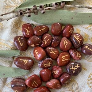 Puede incluir: Un conjunto de 20 piedras de jaspe rojo con runas doradas inscritas en cada una. Las piedras est&aacute;n pulidas y tienen un acabado liso y brillante.