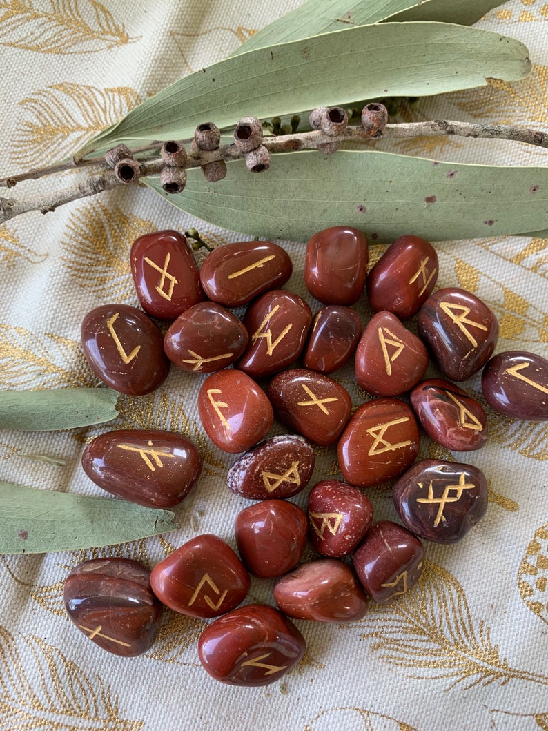 Puede incluir: Un conjunto de 20 piedras de jaspe rojo con runas doradas inscritas en cada una. Las piedras est&aacute;n pulidas y tienen un acabado liso y brillante.