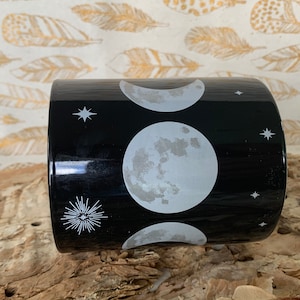 May include: Black ceramic mug with a white moon and stars design. The moon phases are depicted in the design.