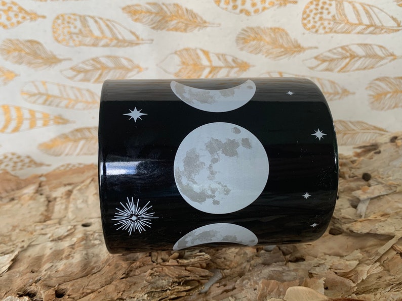 May include: Black ceramic mug with a white moon and stars design. The moon phases are depicted in the design.