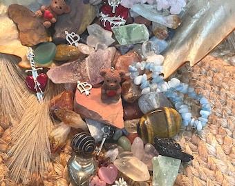 May include: A collection of crystals, stones, and charms in a seashell. The collection includes a variety of colors, shapes, and sizes, including clear quartz, amethyst, rose quartz, tiger's eye, and green aventurine. There are also several charms, including a heart with a sword, a key, and a hand.