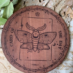 K&ouml;nnte beinhalten: Ein runder Holz-Kartenhalter f&uuml;r die Karte des Tages mit einem Pentagramm und einem Mottiv. Der Text "CARD OF THE DAY" ist um den Rand des Halters graviert. Der Text "YISKA" ist am Boden des Halters graviert.