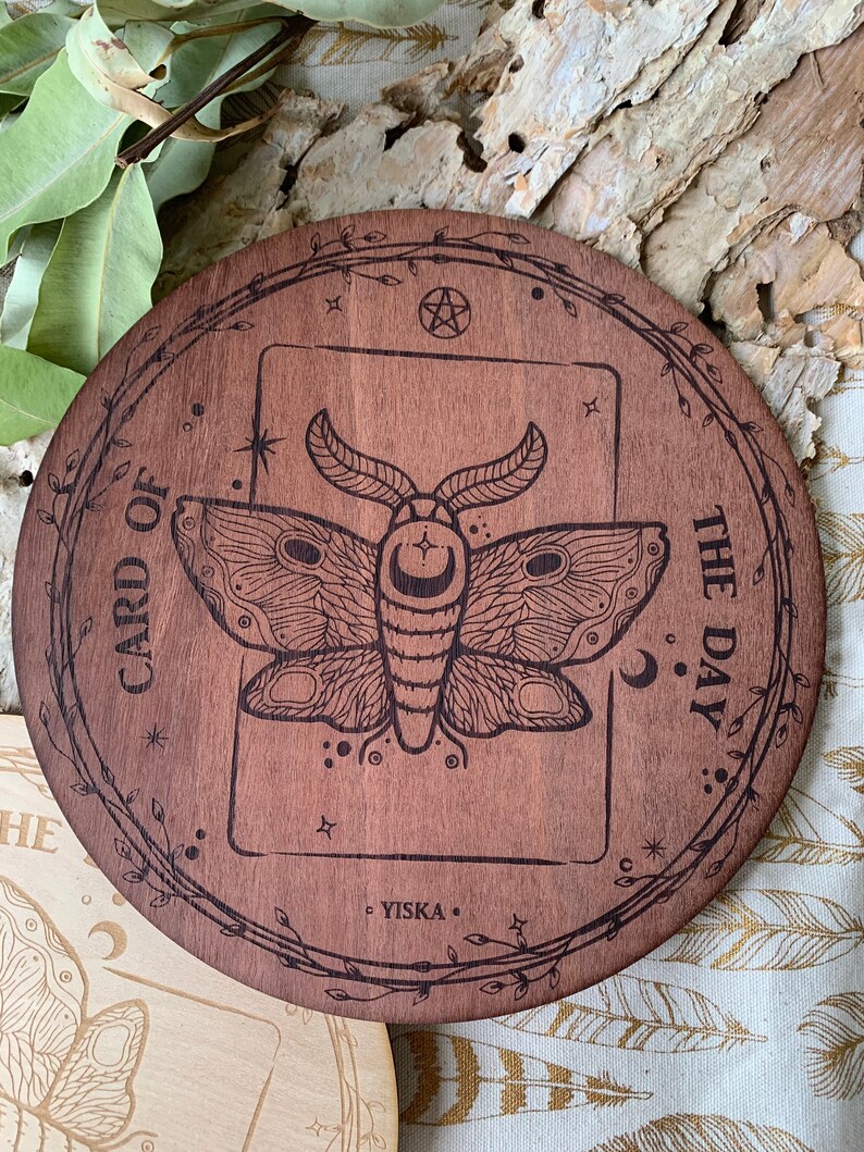 K&ouml;nnte beinhalten: Ein runder Holz-Kartenhalter f&uuml;r die Karte des Tages mit einem Pentagramm und einem Mottiv. Der Text "CARD OF THE DAY" ist um den Rand des Halters graviert. Der Text "YISKA" ist am Boden des Halters graviert.