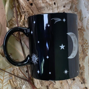 May include: Black ceramic mug with a white crescent moon, stars, and a shooting star design.