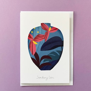 May include: A greeting card featuring a blue vase with pink and yellow flowers and green leaves. The text "Sending Love" is printed on the card.