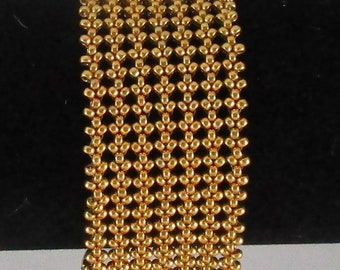 May include: A gold-colored beaded bracelet with a geometric pattern. The bracelet is made of small, round beads that are woven together to create a delicate and intricate design.