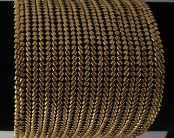 May include: A gold-colored bracelet made of small, square beads woven together in a herringbone pattern.
