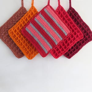 Könnte beinhalten: Fünf handgefertigte Topflappen aus Häkelarbeit in Braun-, Orange-, Rot- und Burgundertönen, jeweils mit einer Schlaufe zum Aufhängen. Ein Topflappen hat rote, rosa und graue Streifen. Die anderen haben strukturierte Muster.
