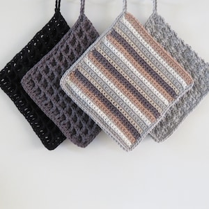 Może przedstawiać: Cztery kwadratowe podkładki pod garnki z szydełkowymi wzorami w kolorze czarnym, szarym i w paski wiszą na białym tle. Podkładka w paski ma naprzemienne rzędy bieli, beżu i szarości. Każda podkładka ma pętlę do zawieszenia.