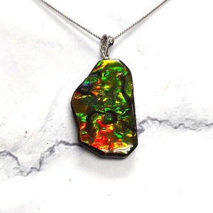 May include: A silver chain necklace with a large, iridescent, green, red, and gold gemstone pendant. The pendant is a natural, irregular shape.