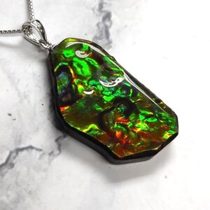 May include: A green, iridescent, gemstone pendant with a silver chain. The pendant is a natural, rough-cut stone with a unique, swirling pattern.