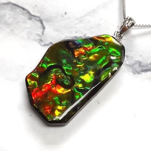 May include: A silver pendant necklace featuring a large, iridescent, green, red, and gold ammonite fossil. The fossil is set in a silver bezel and hangs from a silver chain.