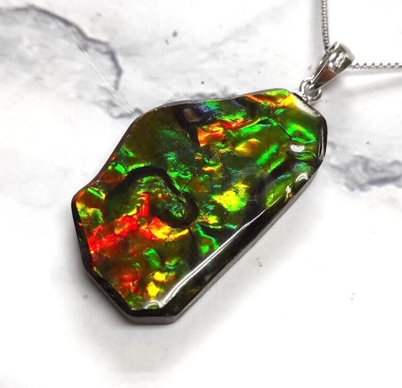May include: A silver pendant necklace featuring a large, iridescent, green, red, and gold ammonite fossil. The fossil is set in a silver bezel and hangs from a silver chain.