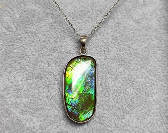 May include: A silver chain necklace with a large, oval-shaped pendant featuring a green, iridescent gemstone.
