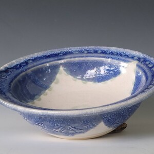 May include: A white ceramic bowl with a blue glaze. The bowl has a scalloped edge and a decorative pattern on the bottom.