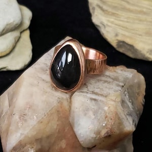 Puede incluir: Un anillo de piedra negra en forma de lágrima engastado en una banda de cobre martillado.