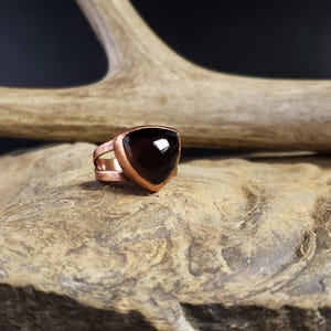 Puede incluir: Un anillo de cobre con una piedra preciosa negra triangular engastada en el centro.