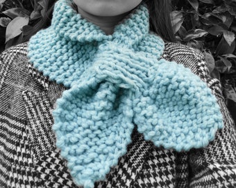 May include: A light blue knitted scarf with a loose, textured weave. The scarf is folded in half and draped around the neck.
