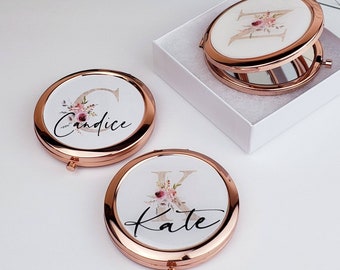May include: Two rose gold compact mirrors with floral designs and personalized names. The mirror on the left says "Candice" and the mirror on the right says "Kate".