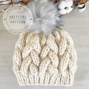 May include: A white knitted beanie with a cable knit pattern and a fluffy pom pom on top. The beanie is on a light wood background. The text "Knitting Pattern" is in a circle around the beanie.