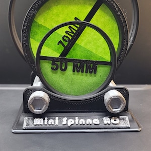 Puede incluir: Un mini spinner impreso en 3D negro y verde con tres círculos concéntricos. Los círculos están etiquetados con las medidas 90 mm, 50 mm y 10 mm. La base del spinner es negra con el texto "mini spinner RC" en letras plateadas.