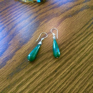 Op de afbeelding: Zilveren oorhangers met druppelvormige, levendige groene stenen. De oorbellen hebben een eenvoudig ontwerp, met een zilveren haak en een kleine zilveren kraal. De stenen zijn ongeveer 2,5 cm lang.